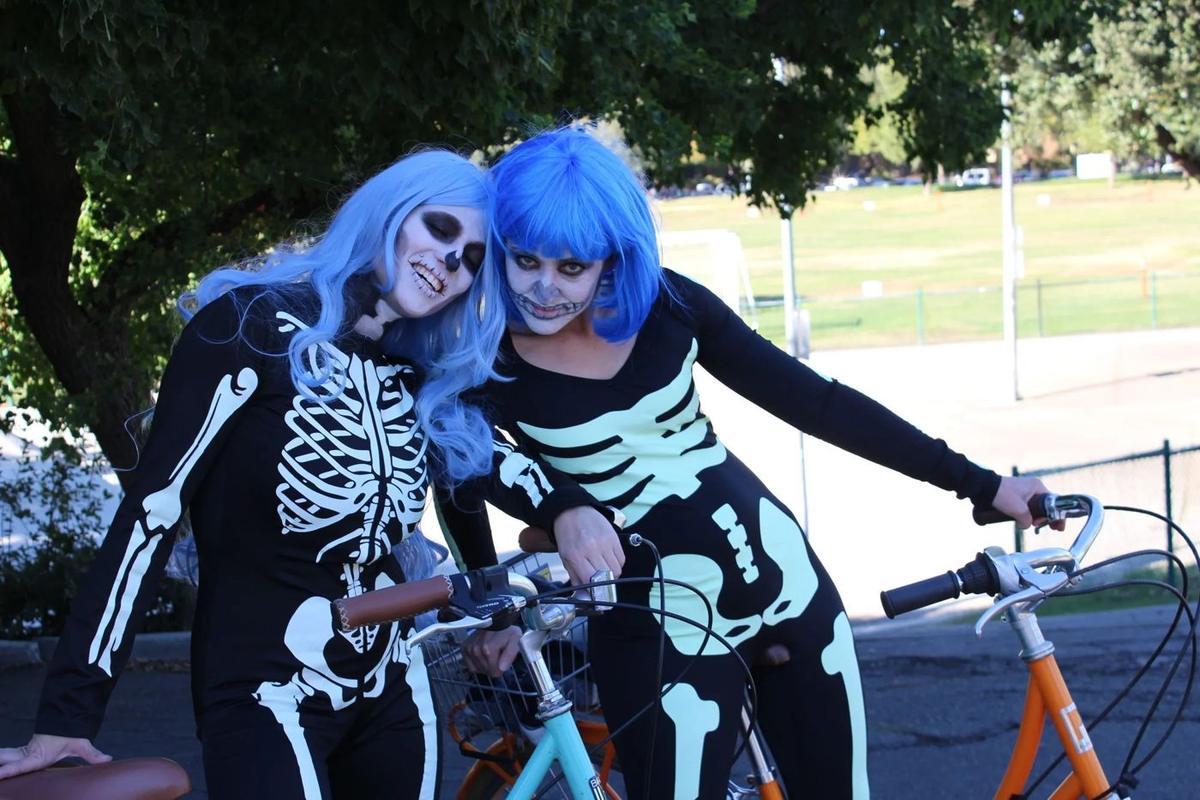 Two riders in blue wigs and skeleton face paint on their bikes