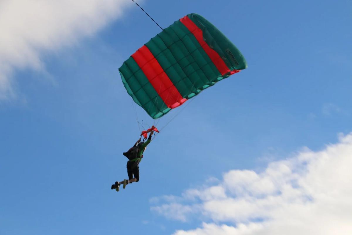 A skydiver under a green and red canopy over the park